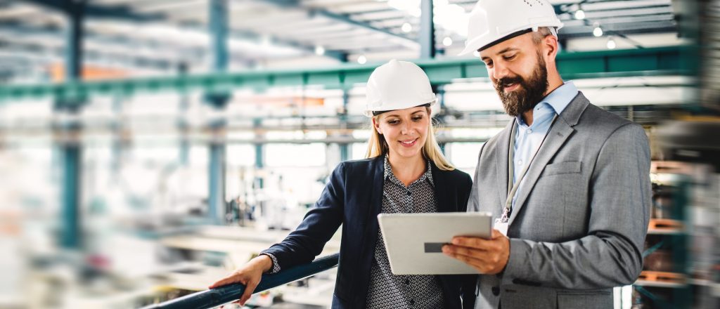 Professional male and female engineers in a factory location using a tablet to discuss business activity